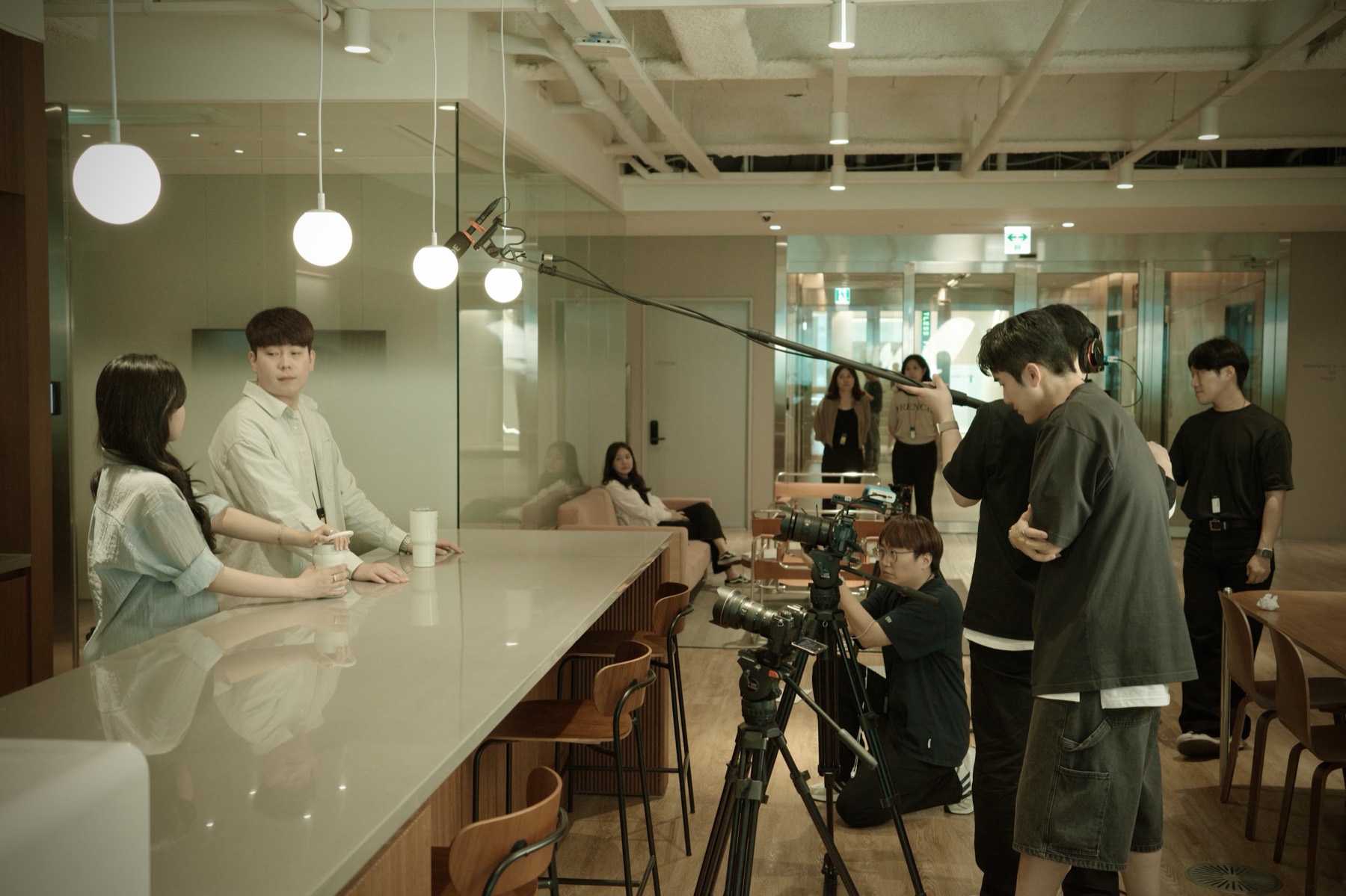 카페 공간에서 배우 두 명을 붐마이크와 카메라로 촬영하는 브랜디드 콘텐츠 현장